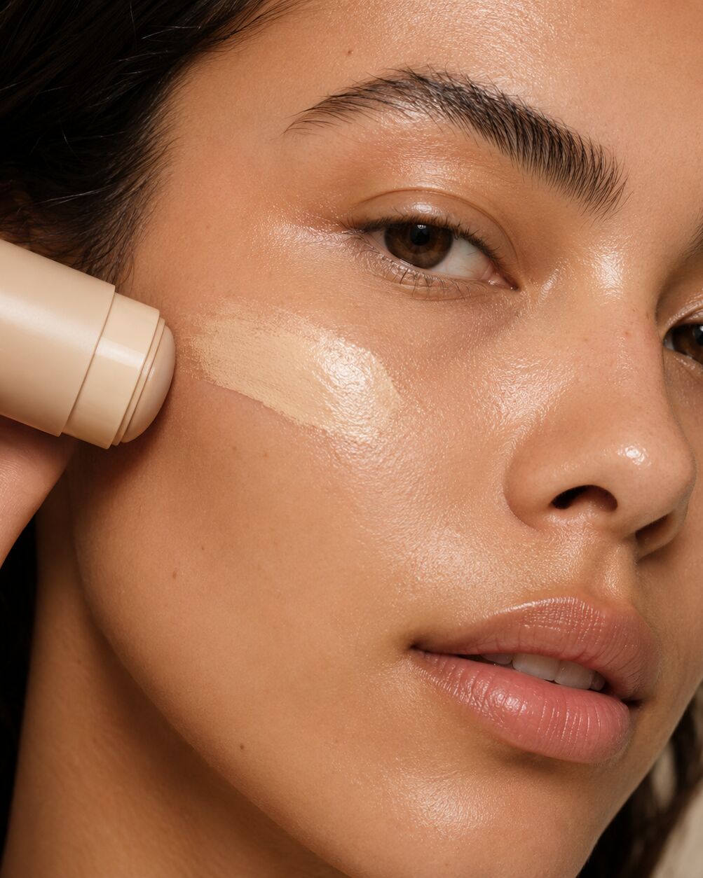 Mulher de pele quente e radiante aplicando base em bastão da Inteira Cosméticos, em luz natural suave